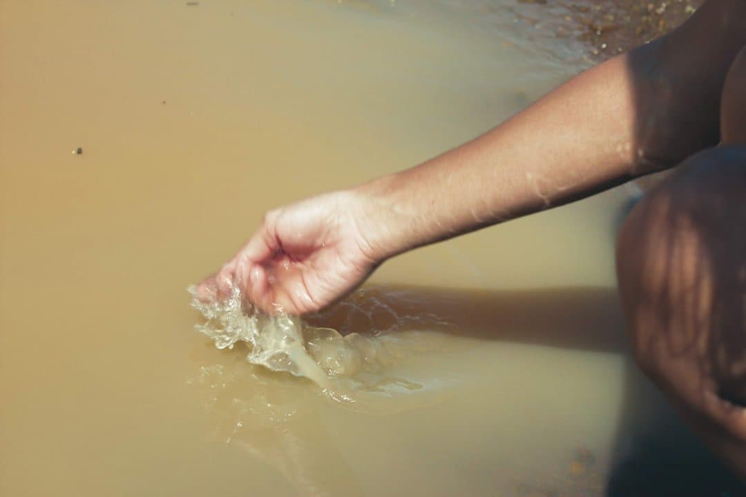 Mão filtrando água lamacenta com detritos em situação de crise hídrica